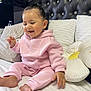 Tanisha is registered to the contest to win money with this photo: baby, bed, black_headboard, child, cozy, cute, feet, flower_pillow, hand, happy, headboard, hoodie, indoor, infant, pants, pillow, pink_clothing, sitting, smiling, white_bed