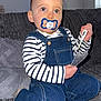 toddler, child, pacifier, striped_clothing, denim_overalls, blue_eyes, thermometer, couch, gray_couch, indoor, kneeling, baby, person, home, soft_furniture, cute, portrait, casual_clothing, small_child, curious