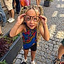 Elaïa participe au concours pour gagner de l'argent avec cette photo : child, glasses, braids, pigtails, street, cobblestone, plants, people, shoes, shorts, sneakers, colorful, summer, outdoor, sidewalk, fashion, playful, portrait, happy, casual