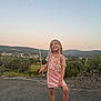 child, girl, balloon, braids, pink_dress, sandals, outdoor, sunset, sky, hills, fence, pavement, smile, happy, nature, landscape, person, standing, holding, casual_clothing