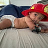 Zayn joined the competition — help win amazing prizes! baby, infant, child, diaper, firefighter_helmet, red_hat, bed, bedroom, lying_down, portrait, face, eyes, smiling, curious, indoors, blanket, bedding, toy, bracelet, firefighter