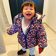 Luna participe au concours pour gagner de l'argent avec cette photo : toddler, child, smiling, jacket, floral_pattern, indoor, door, tile_floor, happy, holding_object, brown_shoes, pants, cute, standing, warm_clothing, short_hair, playful, young, person, portrait
