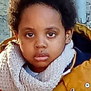 Emmanuel Jess a rejoint le concours — aidez-le/la à gagner de superbes lots ! child, face, scarf, jacket, yellow_jacket, curly_hair, outdoor, portrait, young_child, winter_clothing, serious_expression, person, standing, casual_photo, textured_wall, warm_clothing, close_up, head_and_shoulders, brown_skin