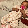 baby, bed, bedroom, blanket, cozy, curly_hair, dark_skin, floral_pajamas, indoors, infant, lying_down, pacifier, photography, pillow, pink_clothing, portrait, relaxed, resting, sleeping, socks