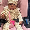Roslynn is registered to the contest to win money with this photo: baby, infant, child, portrait, car_seat, pink, hat, floral_outfit, onesie, pacifier, beads, seatbelt, sitting, indoors, close_up, face, eyes, baby_clothing, transportation, safe