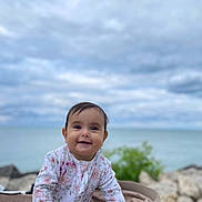 Amina joined the competition — help win amazing prizes! baby, beach, cloud, coast, face, happy, head, landscape, nature, outdoors, person, photography, portrait, rock, sea, shoreline, sitting, sky, smile, water