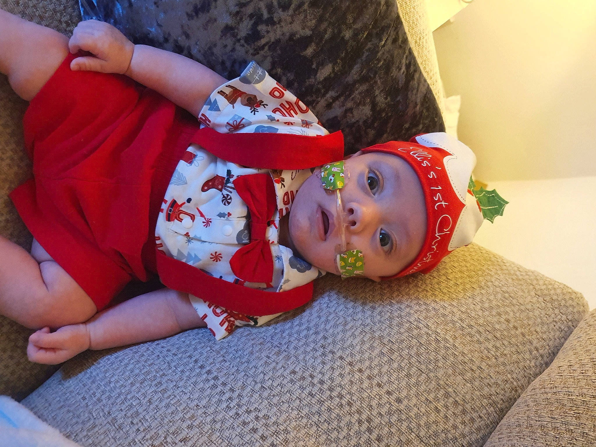 Ellis is registered to the contest to win money with this photo: baby, baby_toddler_clothing, carmine, child, christmas_eve, comfort, event, facial_expression, flooring, fun, happy, hat, headgear, headwear, human_leg, pattern, person, room, smile, thigh