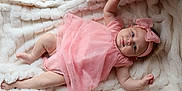 Milani is registered to the contest to win money with this photo: baby, infant, pink_dress, headband, bow, blanket, crib, sleepwear, lying_down, cute, child, soft_texture, cozy, indoor, portrait, one_person, newborn, skin, hands, feet
