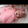 Milani is registered to the contest to win money with this photo: baby, infant, pink_dress, headband, bow, smiling, happy, lying_down, blanket, soft_texture, cute, child, portrait, young_child, toddler, indoors, baby_girl, apparel, fabric, face