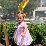 ball, caution_sign, child, curly_hair, dress, golden, greenery, outdoor, plants, portrait, purple, sandals, shoes, sidewalk, statue, summer, sunlight, toddler, wet_floor_sign, young_child