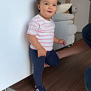 Camélia a rejoint le concours — aidez-le/la à gagner de superbes lots ! toddler, child, indoor, person, standing, striped_shirt, navy_pants, sneakers, pony_tail, floor, adult, support, smile, happy, wood_floor, tile_floor, bracelet, couch, home, light