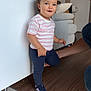 toddler, child, indoor, person, standing, striped_shirt, navy_pants, sneakers, pony_tail, floor, adult, support, smile, happy, wood_floor, tile_floor, bracelet, couch, home, light
