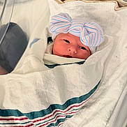 Isabella is registered to the contest to win money with this photo: newborn, baby, infant, child, face, eyes, hospital, bassinet, swaddle, blanket, bow, hat, striped, pastel, portrait, lying_down, cozy, indoors, medical_setting, newborn_photography