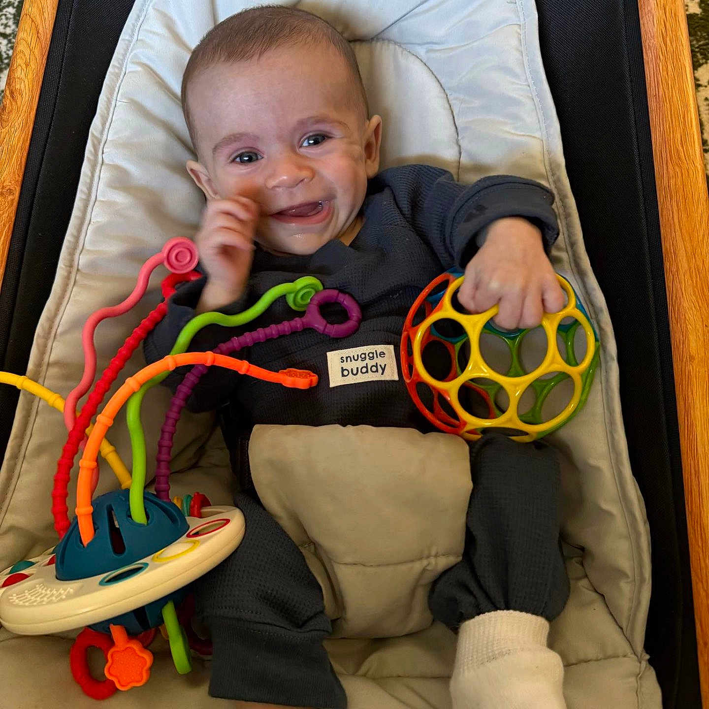 Huxley is registered to the contest to win money with this photo: baby, baby_chair, child, clothing, colorful, cushion, cute, fabric, face, footwear, hand, happy, indoor, infant, person, play, seat, smiling, sock, toy