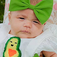 Layla is registered to the contest to win money with this photo: baby, child, face, headband, green_bow, avocado_patch, white_clothing, cute, portrait, closeup, infant, expression, fashion, baby_fashion, outdoor, grass, blanket, texture, skin, person