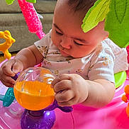Layla joined the competition — help win amazing prizes! baby, child, toy, pink, purple, orange, green, indoor, activity_center, playful, couch, clothing, face, hand, sitting, person, closeup, infant, cute, exploring