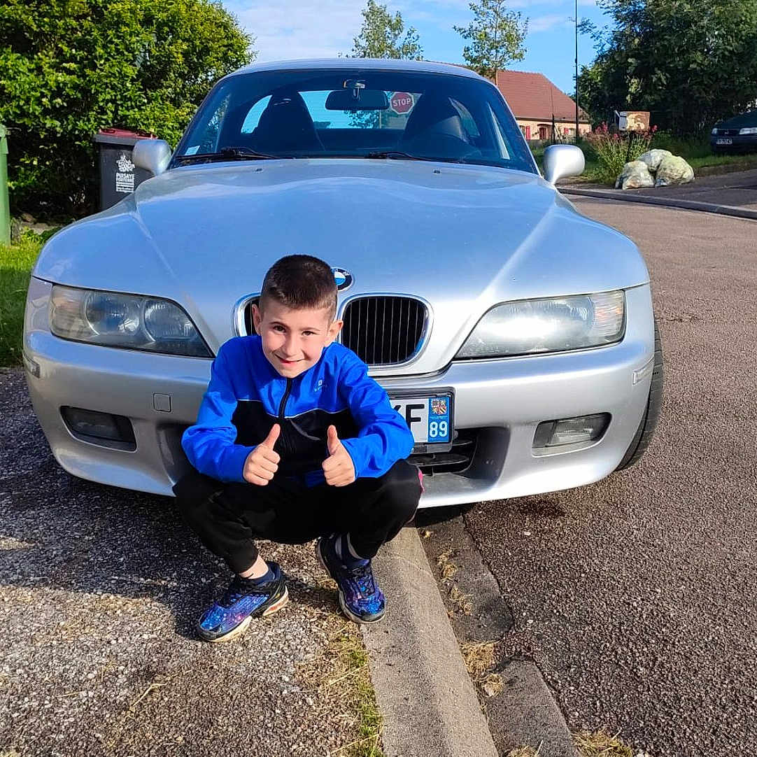 Maël participe au concours pour gagner de l'argent avec cette photo : asphalt, blue_jacket, bmw, boy, car, child, curb, daytime, grass, number_2, parking, residential_area, silver_car, smiling, sneakers, street, suburban, sunny, thumbs_up, trash_bin