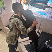 Bluey is registered to the contest to win money with this photo: child, dog, hug, couch, indoor, curtain, cartoon, black_dog, affection, light, window, floor, clothing, sleeves, pants, footwear, back, pet, furniture, home
