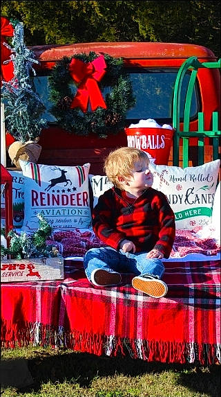 Kolton is registered to the contest to win money with this photo: advertising, christmas, christmas_decoration, christmas_eve, christmas_ornament, christmas_tree, event, fictional_character, green, holiday, jacket, lap, magenta, ornament, pattern, person, santa_claus, sitting, tartan, toddler