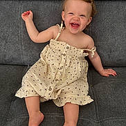 Esmeralda a rejoint le concours — aidez-le/la à gagner de superbes lots ! toddler, child, smiling, laughing, dress, hair_clip, barefoot, sitting, couch, grey_fabric, cute, happy, indoors, portrait, baby, one_person, casual, clothing, young_child, natural_light