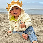 Thomas joined the competition — help win amazing prizes! toddler, child, beach, sand, sweater, hood, crown, thumbs_up, happy, smiling, barefoot, ocean, sky, cloudy, outdoor, playing, casual_clothing, cute, portrait, young_child