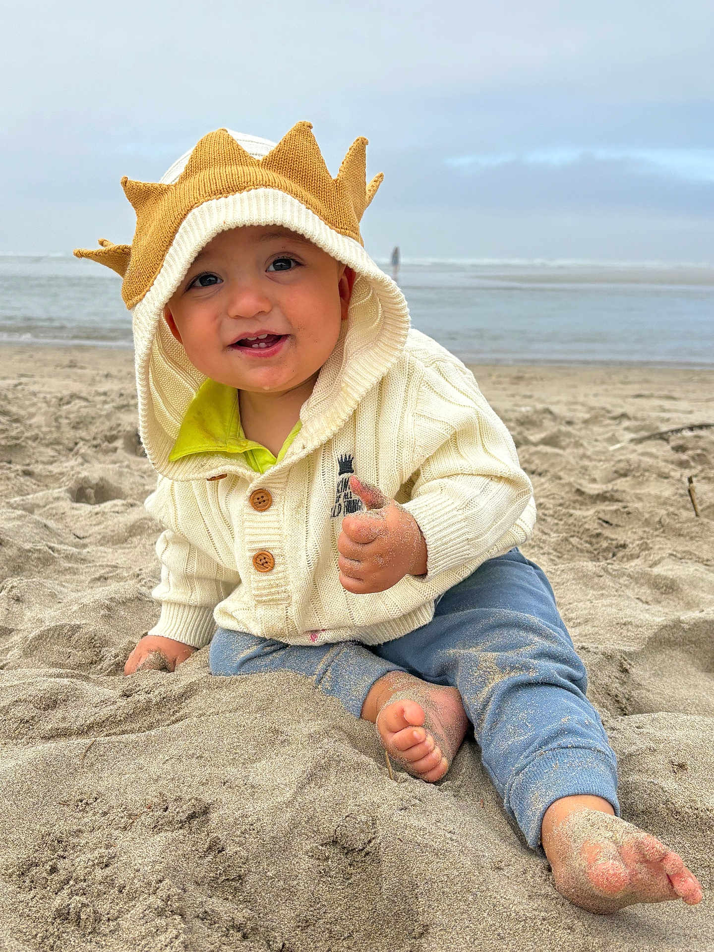 Thomas joined the competition — help win amazing prizes! toddler, child, beach, sand, sweater, hood, crown, thumbs_up, happy, smiling, barefoot, ocean, sky, cloudy, outdoor, playing, casual_clothing, cute, portrait, young_child