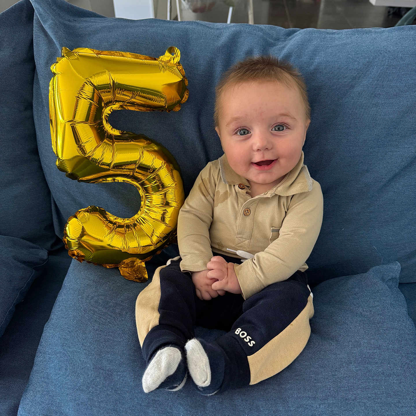 Lewis participe au concours pour gagner de l'argent avec cette photo : baby, balloon, blue_couch, celebration, child, clothing, cushion, expression, face, furniture, happy, home, indoors, infant, number_five, person, portrait, sitting, smile, socks