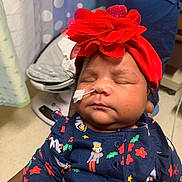 Winter is registered to the contest to win money with this photo: baby, infant, sleeping, headband, flower, medical_tube, tape, navy_blue_clothing, holiday_prints, person_holding, indoor, curtain, baby_rocker, closeup, cute, peaceful, child, newborn, soft_lighting, portrait