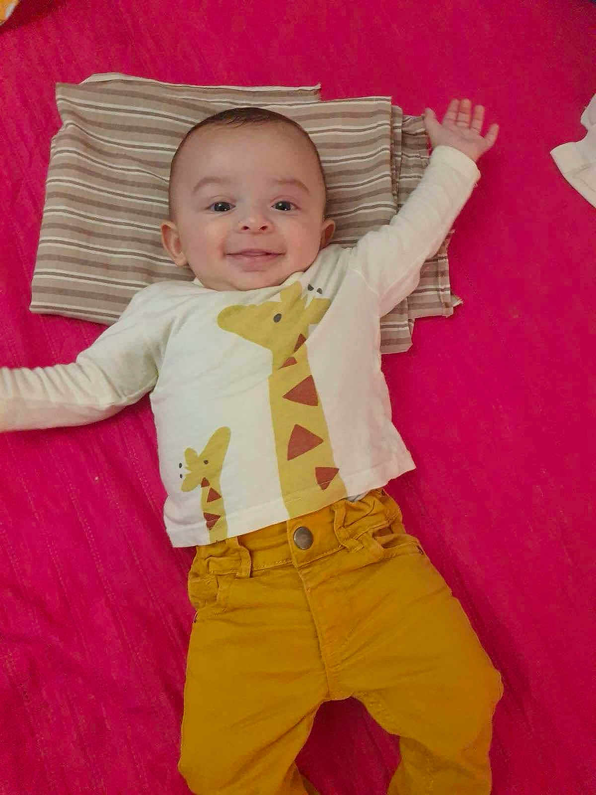 ânes participe au concours pour gagner de l'argent avec cette photo : baby, child, smiling, giraffe_print, yellow_pants, striped_pillow, pink_background, happy, lying_down, infant, cute, clothing, person, portrait, indoors, arms_outstretched, head, face, young_child, resting