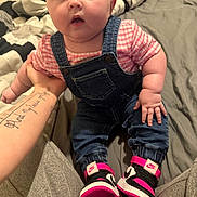 Averlie is registered to the contest to win money with this photo: baby, denim_overalls, pink_shirt, sneakers, nike, tattoo, bed, blanket, person, infant, cute, chubby, hand, footwear, foot, clothing, indoor, portrait, child, casual