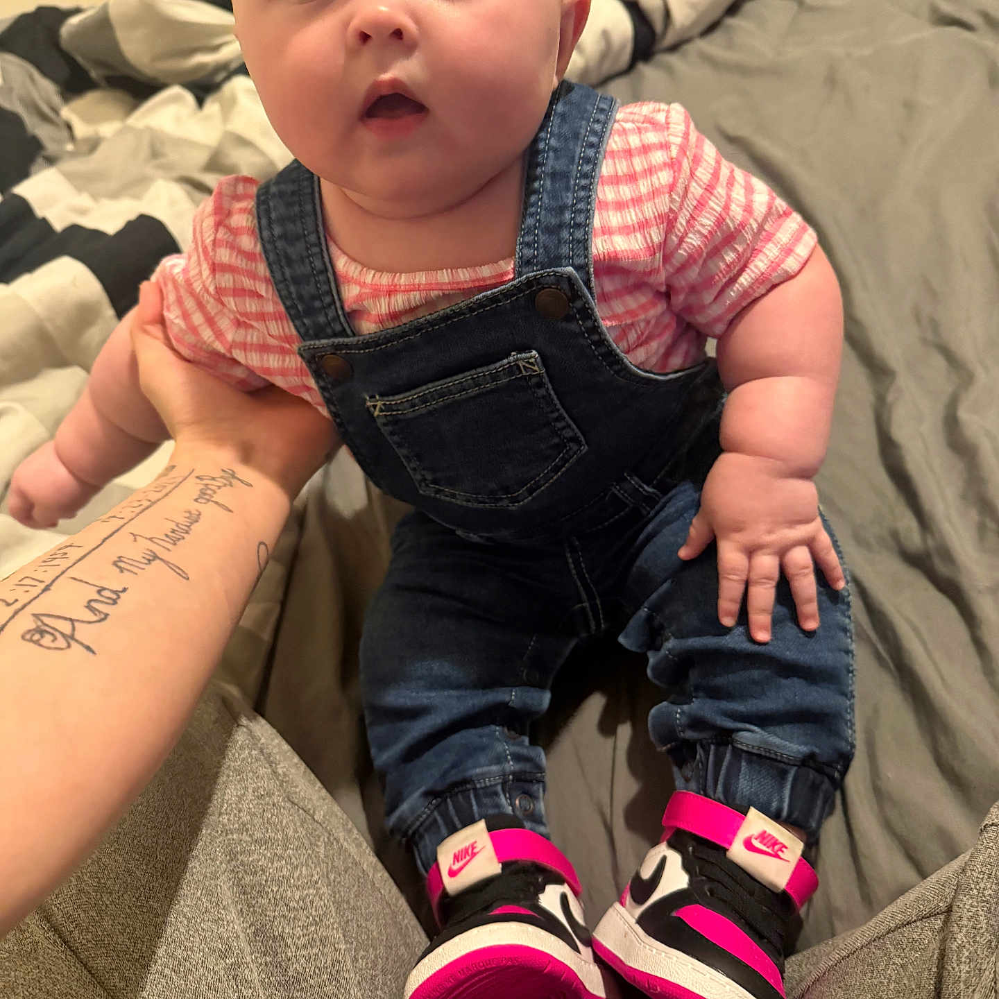 Averlie is registered to the contest to win money with this photo: baby, bed, blanket, casual, child, chubby, clothing, cute, denim_overalls, foot, footwear, hand, indoor, infant, nike, person, pink_shirt, portrait, sneakers, tattoo