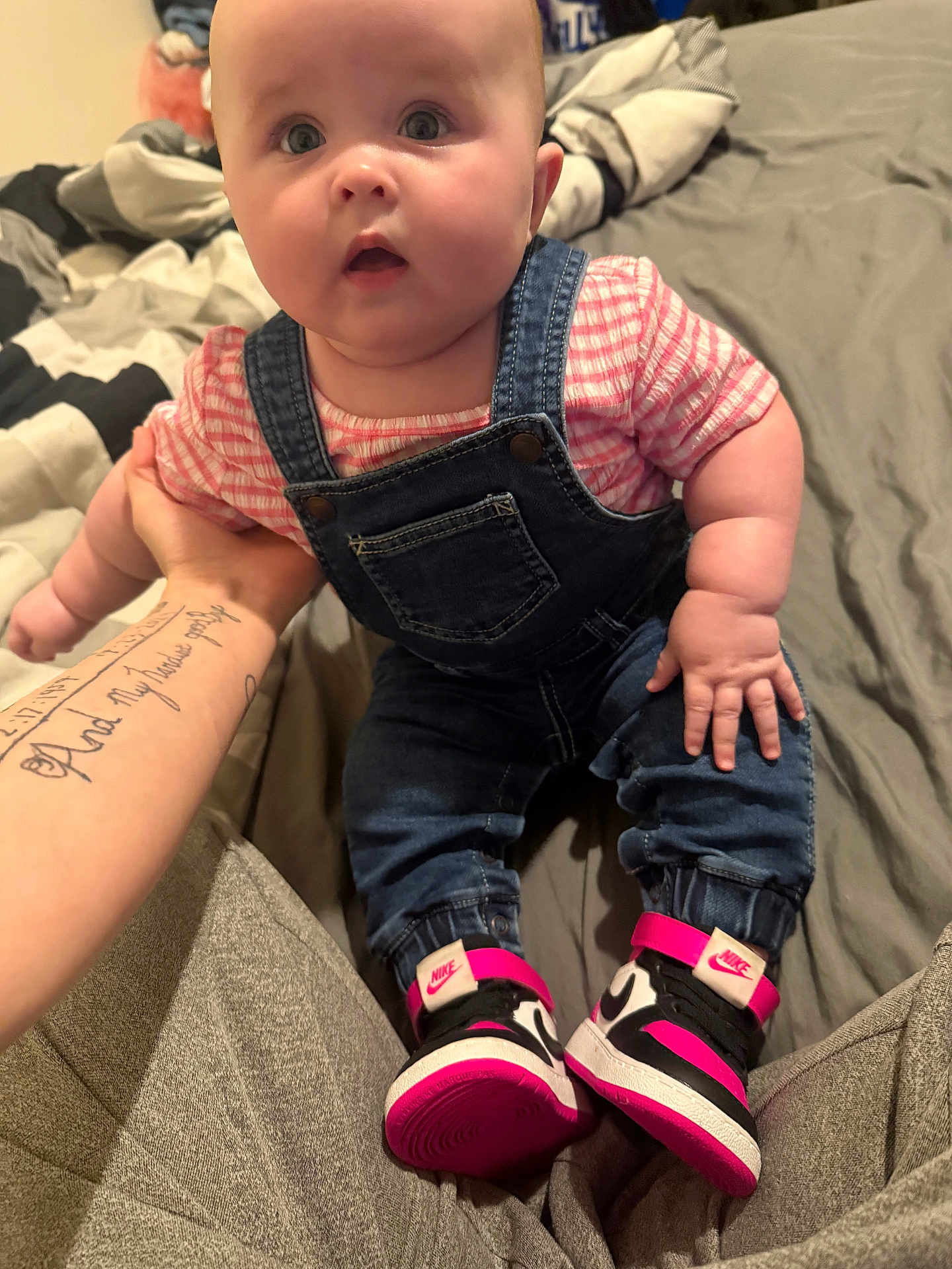 Averlie is registered to the contest to win money with this photo: baby, denim_overalls, pink_shirt, sneakers, nike, tattoo, bed, blanket, person, infant, cute, chubby, hand, footwear, foot, clothing, indoor, portrait, child, casual