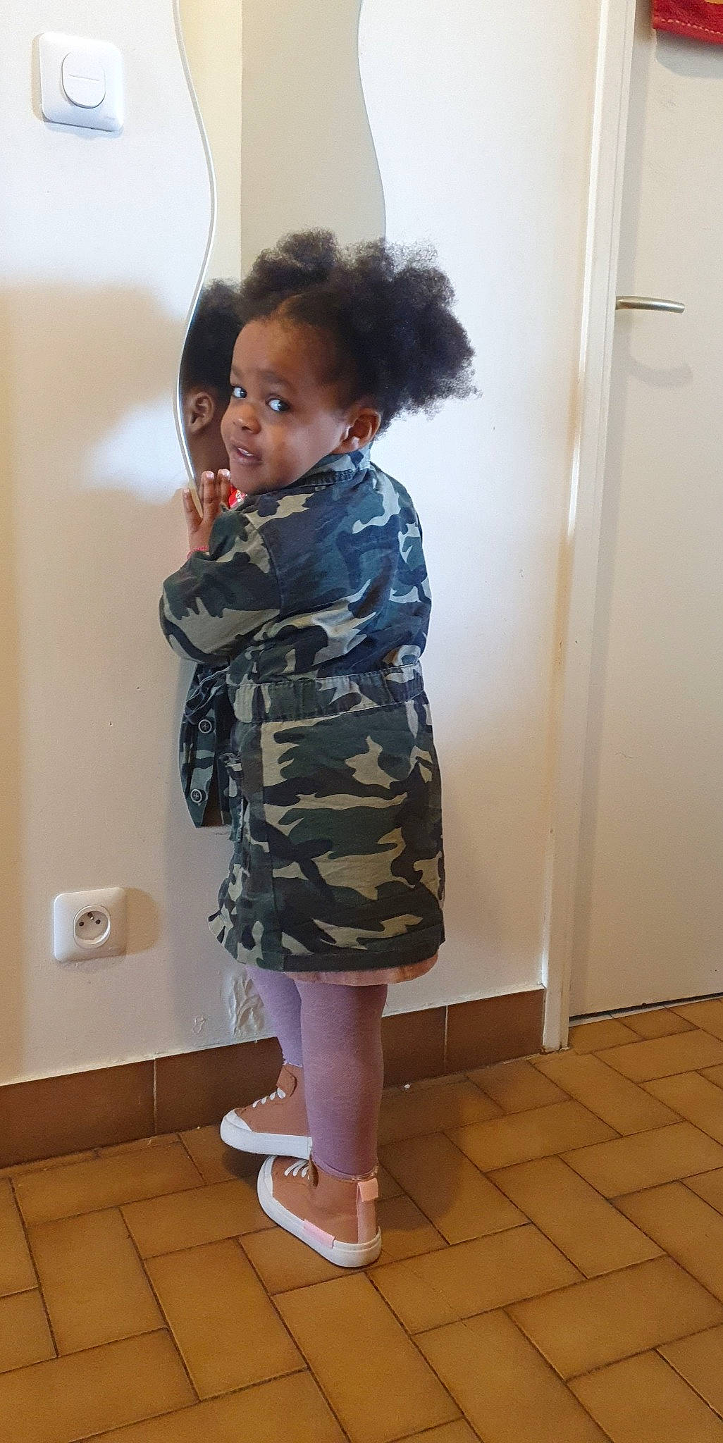 Assiyah participe au concours pour gagner de l'argent avec cette photo : camouflage, door, face, fashion_design, flooring, fun, hair, hardwood, human_leg, knee, military_camouflage, paper_towel, pattern, person, room, shoulder, sleeve, street_fashion, thigh, toddler
