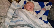 Luca joined the competition — help win amazing prizes! baby, blanket, sleeping, couch, pillow, fabric, camouflage, striped_blanket, child, indoor, resting, cozy, comfort, person, home, soft_texture, peaceful, infant, wrapped, relaxing