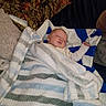baby, blanket, sleeping, couch, pillow, fabric, camouflage, striped_blanket, child, indoor, resting, cozy, comfort, person, home, soft_texture, peaceful, infant, wrapped, relaxing