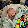 baby, sleeping, blanket, toy, colorful, cushioned_seat, indoor, child, peaceful, soft_texture, striped_blanket, clothing, face, person, resting, comfort, infant, nursery, furniture, home