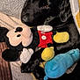 dog, black_dog, plush_toy, mickey_mouse, blanket, cozy, sleepy, pet, stuffed_animal, indoor, comfort, resting, cuddly, soft_texture, toy, animal, cute, relaxation, snuggling, warm