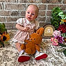 baby, infant, child, plush_toy, bunny, flowers, sunflowers, dress, white_shoes, brick_wall, tablecloth, pink, orange, greenery, indoor, portrait, cute, sitting, decor, 3_months