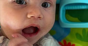 Scout is registered to the contest to win money with this photo: baby, close_up, face, expression, hand, curious, toy, play_mat, colorful, infant, child, skin, mouth, eyes, person, cute, young, indoors, apparel, fingers