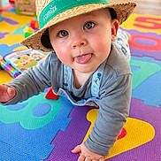 Jules participe au concours pour gagner de l'argent avec cette photo : baby, infant, child, straw_hat, hat, tongue_out, crawling, playmat, foam_mat, colorful, toy, board_book, big_eyes, closeup, portrait, overalls, hand, cheek, indoor, wooden_floor