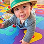 baby, infant, child, straw_hat, hat, tongue_out, crawling, playmat, foam_mat, colorful, toy, board_book, big_eyes, closeup, portrait, overalls, hand, cheek, indoor, wooden_floor