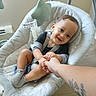 baby, child, swing, cushion, hand_holding, smile, happy, indoor, person, infant, clothing, sock, toy, comfort, home, seat, tattoo, floor, wall, light