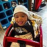 baby, infant, child, smiling, happy, portrait, shopping_cart, red_cart, blanket, hat, clothing, store, shoe_display, shoes, indoor, retail, restaurant, mcdonalds, seated, close_up