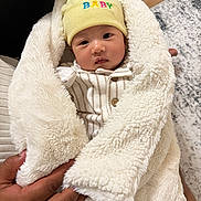 Nityansh is registered to the contest to win money with this photo: baby, blanket, yellow_hat, hands, indoor, floor, rug, wood, cozy, cute, infant, clothing, person, face, portrait, warm, soft, wrapped, newborn, comfortable