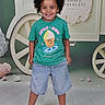 Charly participe au concours pour gagner de l'argent avec cette photo : child, boy, smiling, curly_hair, green_tshirt, denim_shorts, sandals, standing, indoor, background_props, cartwheel, floor, casual_clothing, happy, portrait, playful, cute, fashion, kids_fashion, studio