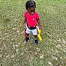 activity, casual_clothing, child, daylight, field, flags, game, grass, outdoor, person, play, red_flag, red_shirt, shorts, sneakers, sports, standing, summer, yellow_flag, young_child