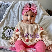 Junie is registered to the contest to win money with this photo: baby, bed, blanket, clothing, face, footwear, furniture, hair, hat, head, homedecor, knitwear, person, photography, portrait, shoe, sitting, sleeve, sweater, text
