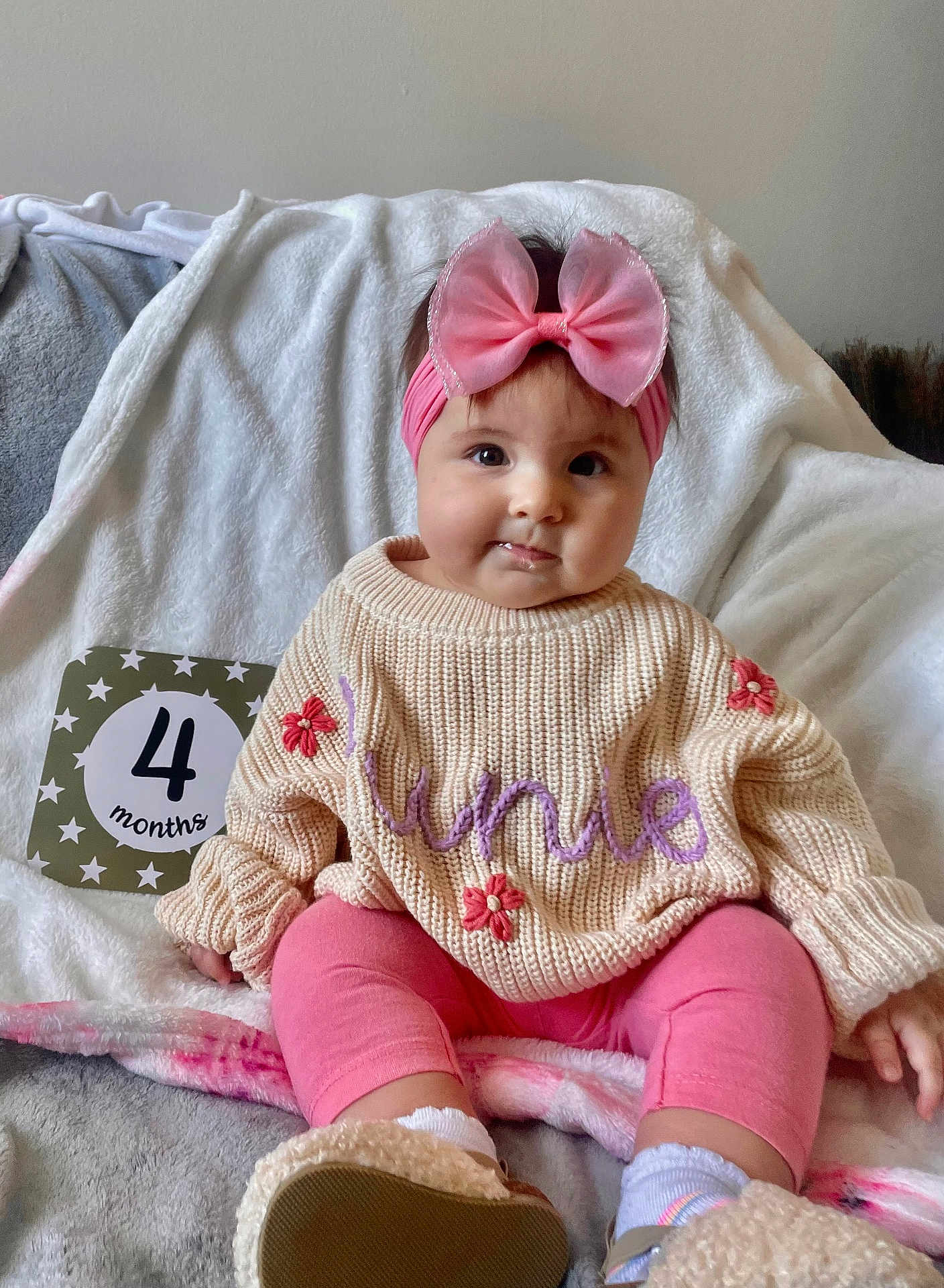 Junie is registered to the contest to win money with this photo: baby, bed, blanket, clothing, face, footwear, furniture, hair, hat, head, homedecor, knitwear, person, photography, portrait, shoe, sitting, sleeve, sweater, text