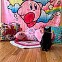 black_cat, cat, toy, butterfly, wooden_floor, kirby, pillows, plush_toy, pink, colorful, rainbow, background, indoor, decor, cute, playful, pet, animal, floor_rug, heart_shaped_pillow