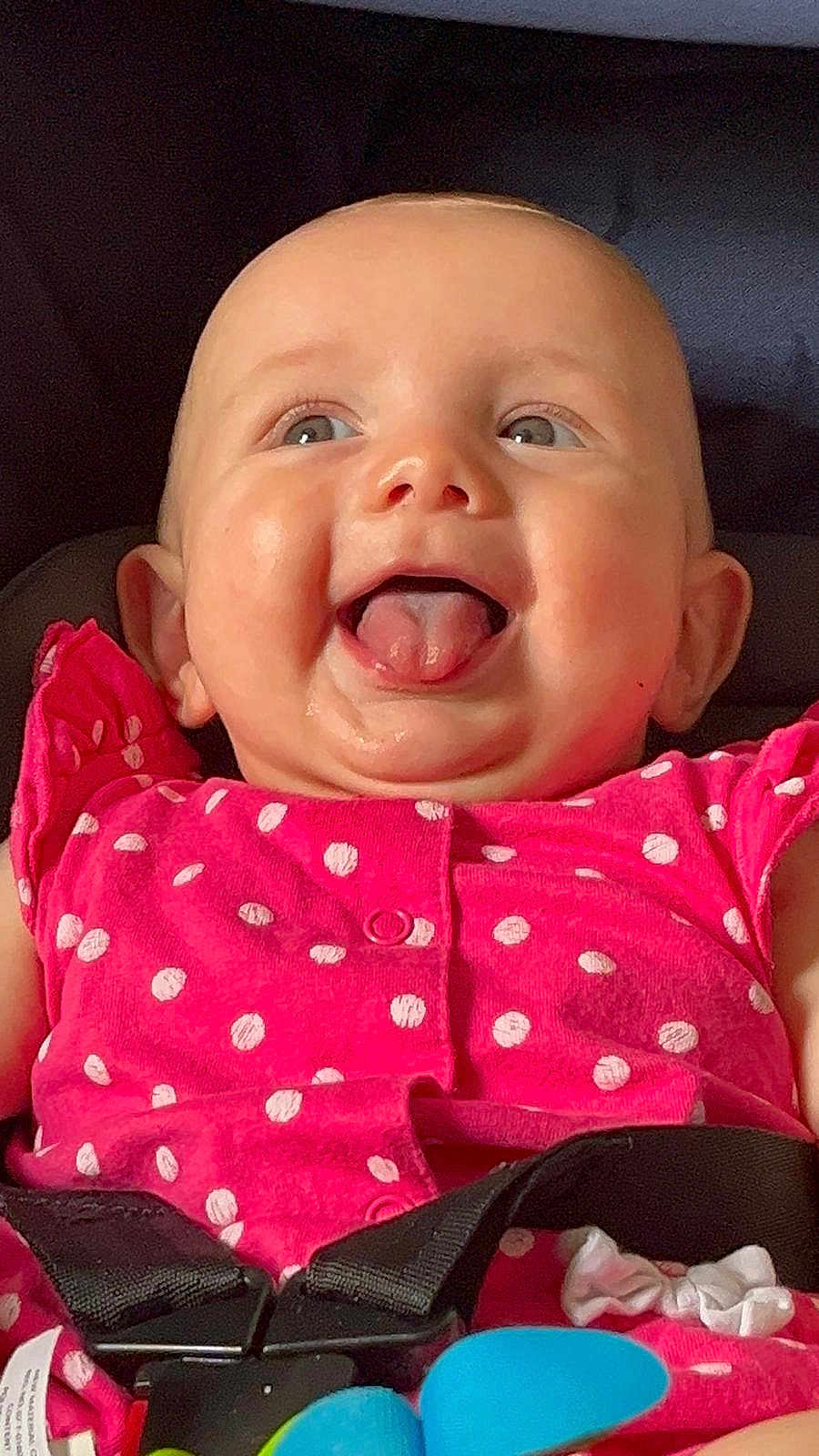 Jasmine is registered to the contest to win money with this photo: baby, infant, child, smiling, tongue_out, pink_clothing, polka_dot, car_seat, safety_harness, happy, cute, face, cheeks, eyes, playful, indoor, closeup, person, seatbelt, toy